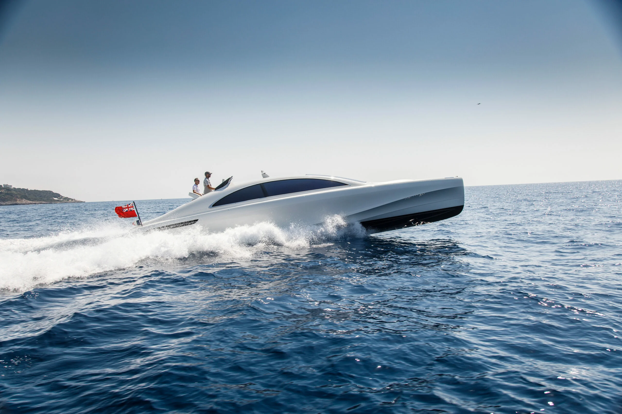 A sleek white speedboat cuts through blue ocean waves under clear sky.